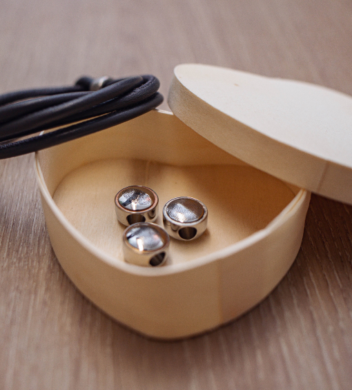 Herzschatulle aus Holz mit drei Fingerprint-Anhängern in Silber. Deckel rechts geöffnet, Armband am linken Rand.