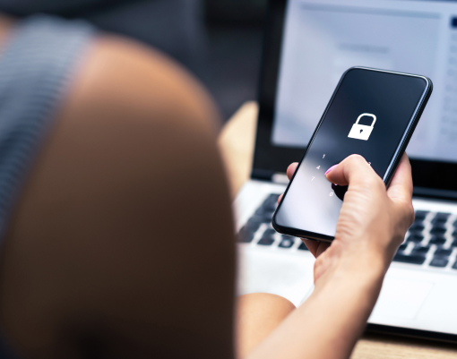 Blick über die Schulter auf Smartphone in der Hand mit Schlosssymbol auf Bildschirm, hinten unscharf Computer