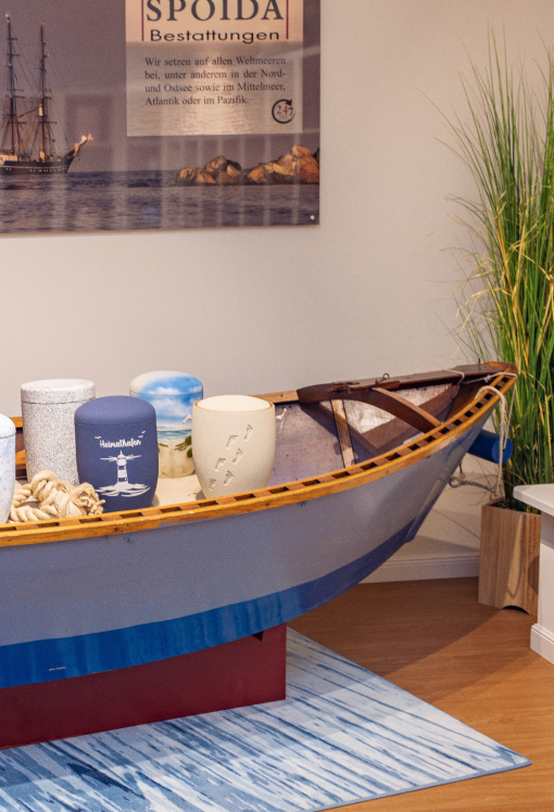 Vorderer Teil eines blauen Ruderbootes, dekoriert mit vier Urnen mit Meeresmotiven und Seil.