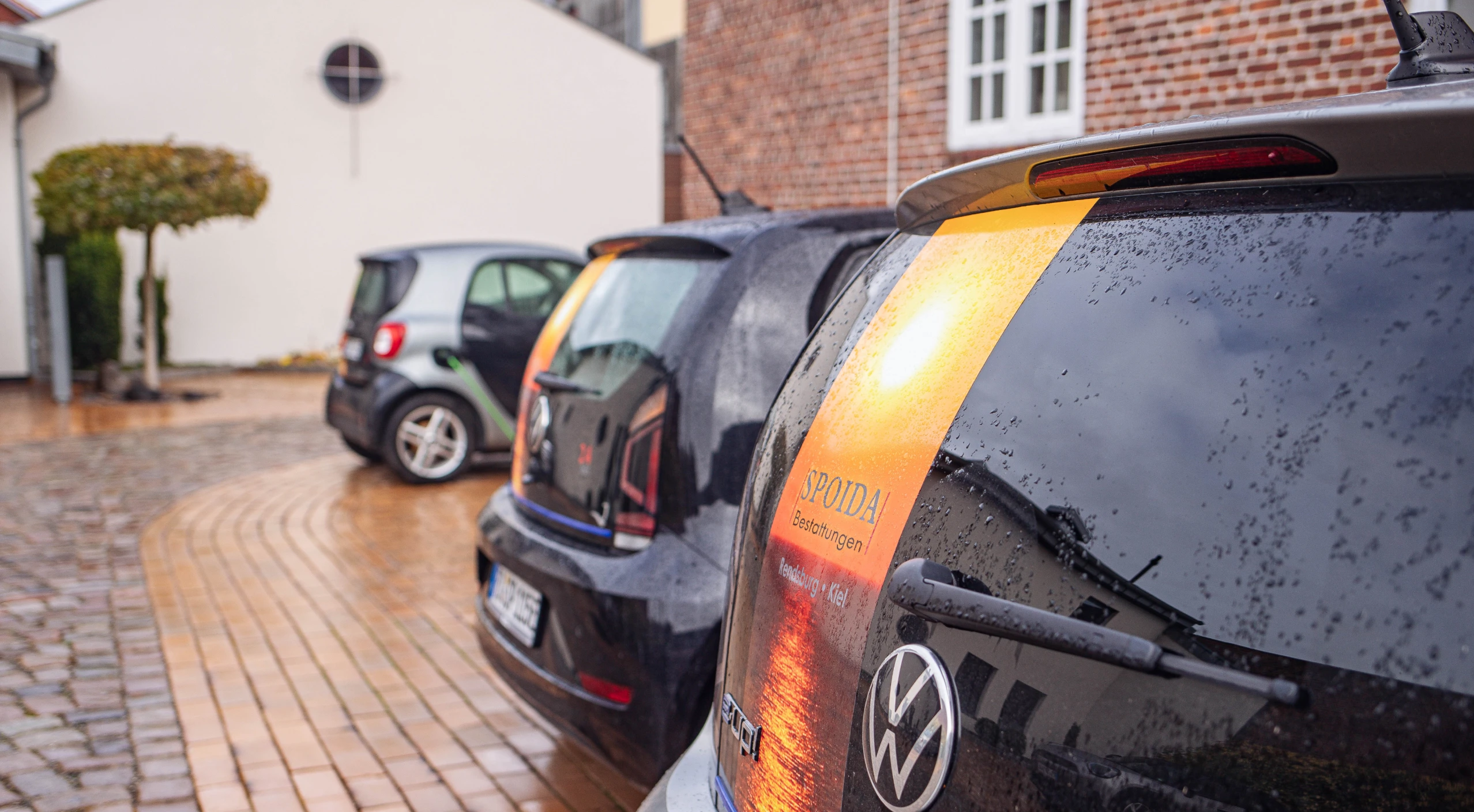 Drei schwarze Firmenfahrzeuge mit Logo auf dem Hof von hinten im Anschnitt.